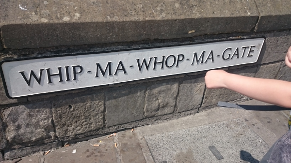 Street name sign in York. It's a white sign with black writing. My childs arm can be seen - it looks like he is punching the sign. 
The street name - Whip-ma-whop-ma-gate. 