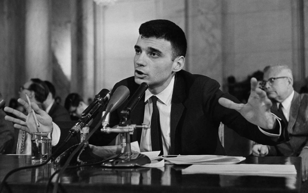 A man wearing a tie, speaking at a press conference.