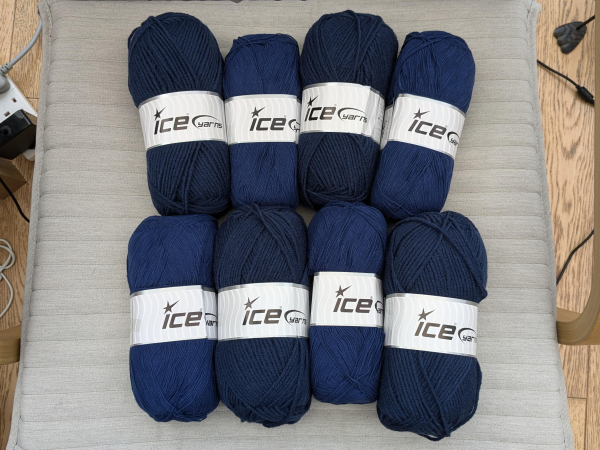 Eight balls of yarn in two similar but different shades of navy blue. They're arranged in two rows of four, alternating between lighter and darker balls. The labels read "Ice Yarns".

They're lying on a neutral coloured chair seat but you can see all the cables on our floor at either side!