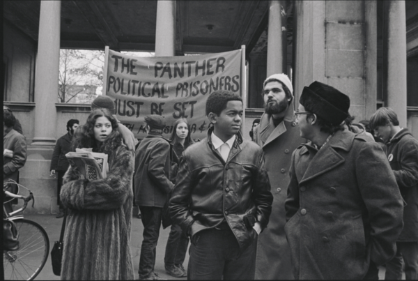 Black and white photo showing a group of GLF protesters standing in front of a banner calling for release of Black Panther political prisoners