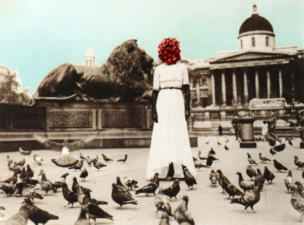 Black and white photo of a woman in a white gown and black gloves with her head obscured by a ball of roses, standing in a square filled with pigeons. The photo has been tinted with some color for the red of the roses and light blue of the sky