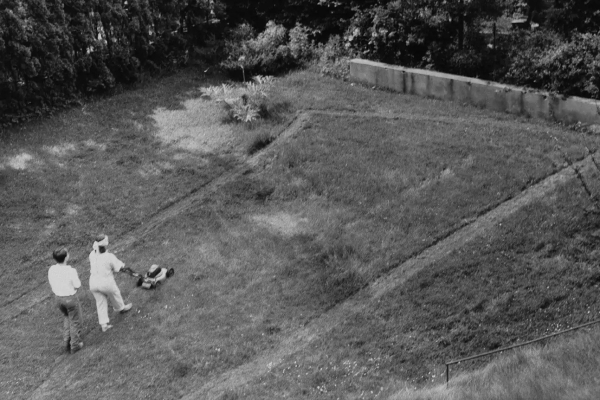 Black and white image of a performance showing the artist and another figure mowing a large grass lawn into a geometric pattern