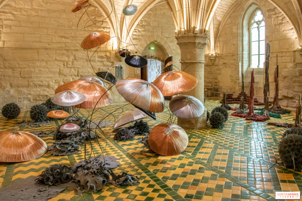 Mushroom-like canopy sculptures made of metallic wire, arranged in a stone-walled room with patterned tile floor and arched ceilings