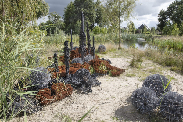 Different forms arranged in a grassy outdoor space, some black and spikey and others brown and curved, others pointed towers