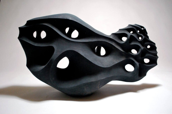 Black abstract sculpture of an oval form with swirling waves and circular openings