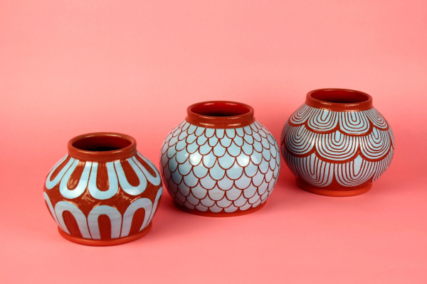 Three round pots with carved curving patterns in burnt orange and blue