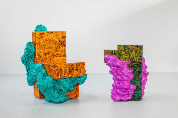 Abstract sculpture furniture, one a bright orange chair with bulbous turquoise forms moving over it, the other a green end table with purple goop moving over its base