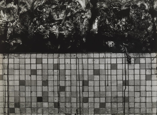 Black and white photo of a square tiled wall with dark textured mud/dirt above it