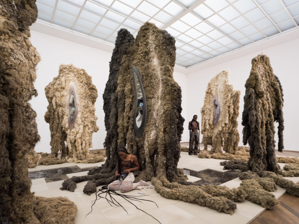 Gallery installation of large textile sculptures in organic, bumpy forms with tendril-like feet erupting from the bases