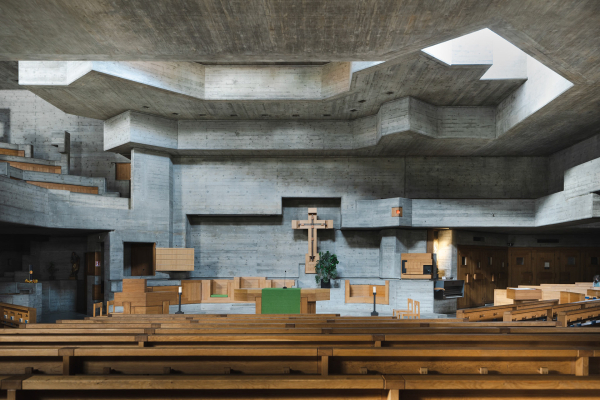 Photo of a Brutalist-style concrete church interior with wooden pews and skylight shining light down