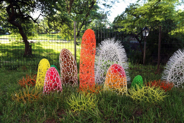 Installation of several freestanding rounded tower structures in different colors, made of interlaced plastic, placed in a grass field