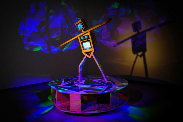 Sculpture of a stick figure posing with their arms out as if skateboarding, with various video screens inlaid within the torso and head