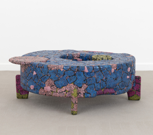 Low rounded sculptural table with a mottled texture and pink and blue freeform tiling with some green and magenta details