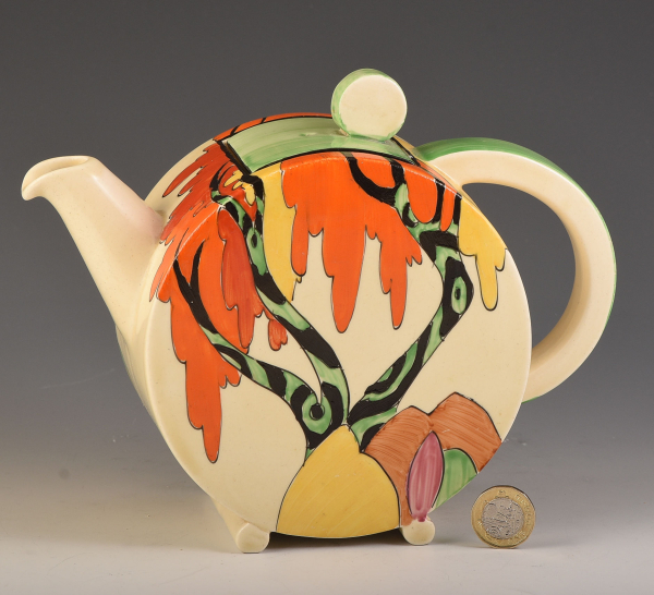 Circular ceramic teapot with a colorful painted design of a semi-abstract tree in green, black, yellow, and orange over a cream base