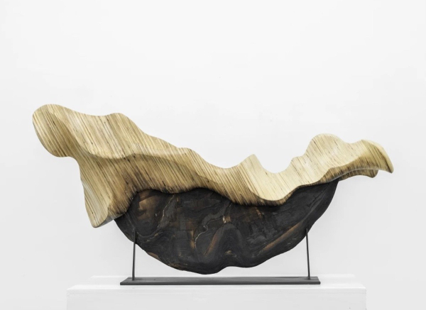 Wooden sculpture of a dark horizontal half-circle shape with a globular lighter brown form spilling over the top