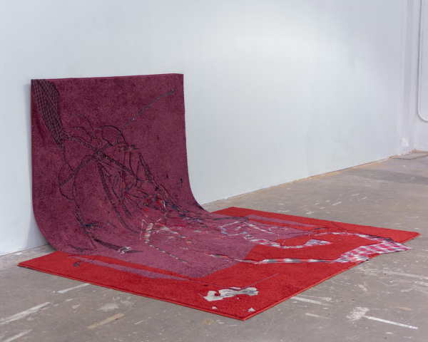 Magenta rug leaning against a wall merging into a red rug on the floor