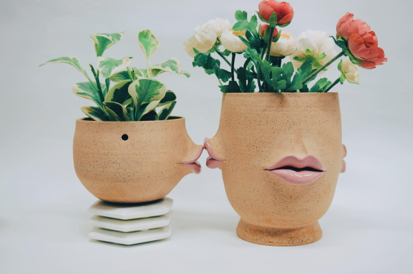 Two ceramic vases holding flowers, with lips sculpted into their centers. One pot is posed as if kissing the other pot