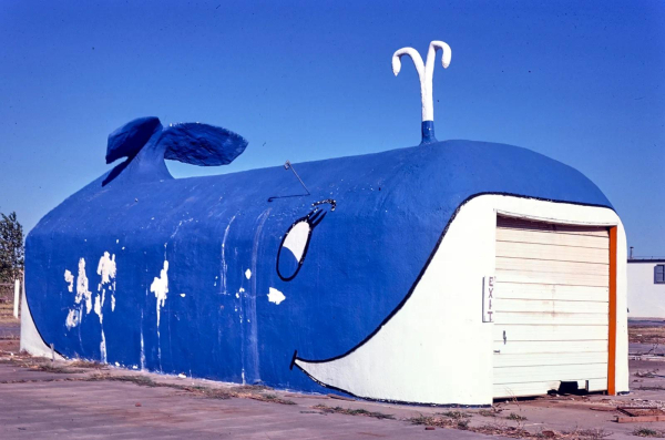 Photo of a long building decorated and sculptured to look like a large blue whale, with a sliding white garage door at the "mouth"