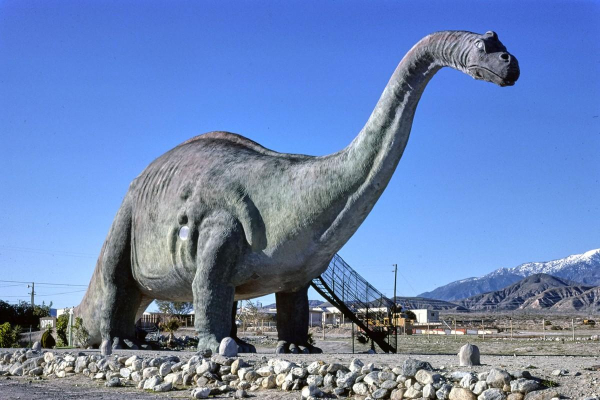 Photo of a large dinosaur sculpture in a rocky landscape, with a set of steps leading up to its midsection