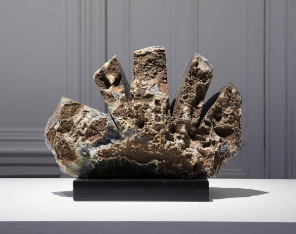 Abstract stone sculpture on a black base, with several finger-like shapes emerging outward and upward from the center