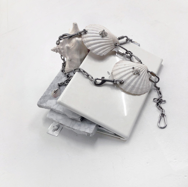 Sculpture of two white shells linked by a metal chain posed atop a half-closed white mac laptop with pieces of marble slid between its screen and keyboard