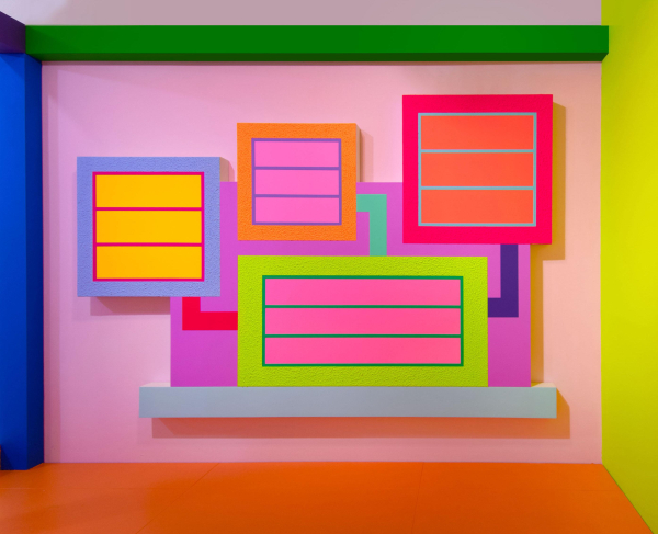 Abstract painting using day-glo paint, with shades of pink, blue, orange, and neon yellow and green, depicting several inset squares, some with horizontal lines and connected with colorful bars. The canvas is shaped around the grouping of squares, with several zig-zag edges. It is displayed in a colorful gallery with a pink wall and orange floor, and bars of green, blue, and purple framing the wall.