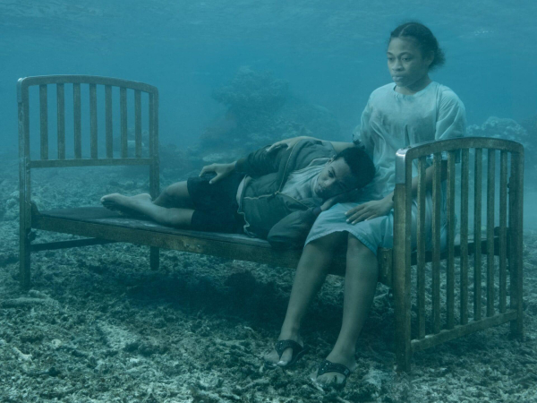 Underwater photo of a woman sitting on a bed frame with a man lying on her lap