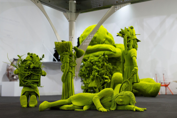 Sculpture of several childlike figures grouped together, the central one is lying on the ground asleep, all entirely in a bright green hue and some with leafy forms 