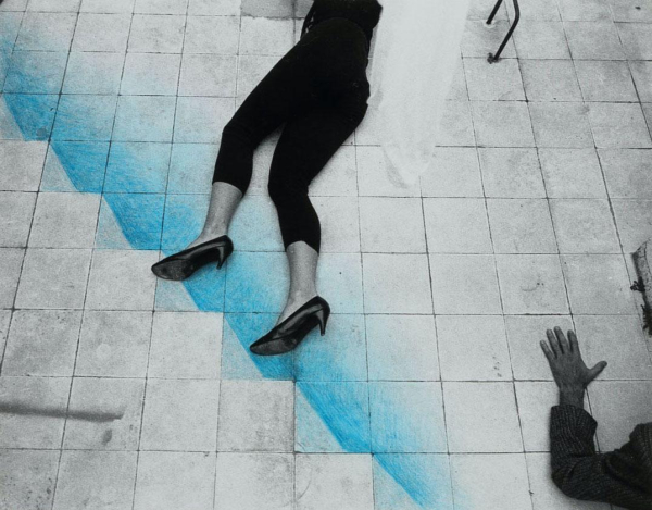 Grayscale image of a woman's legs in black leggings and kitten heels, lying on a tiled floor with blue crayon drawn to create an illusionistic staircase, with a person's arm visible raised in the lower corner