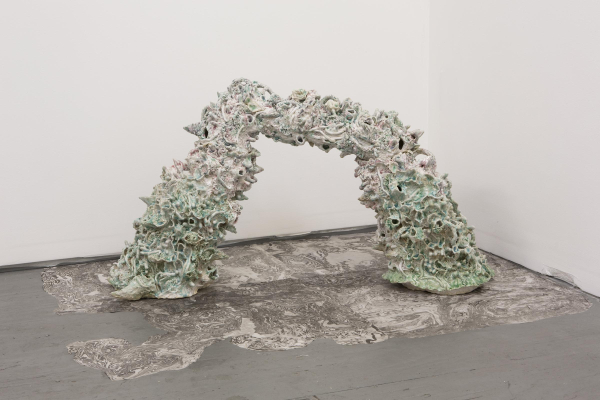 Abstract ceramic sculpture on a gallery floor of a large curving form with various textured elements and pale green and pink glazes