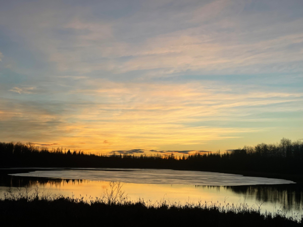 Orange and yellow Sunset sky reflecting on partially ice covered pond 