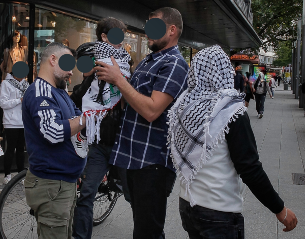 Foto zeigt Teilnehmer einer der wöchentlichen Pro-Palästina-Demos in der Innenstadt von Hannover. Es sind fünf Personen zu sehen. Vier tragen die Kufiya, den in Deutschland sogenannten "Palästinenserschal". Zwei Männer wickeln ein Kleinkind in diesen Schal. Personen sind mit einem grauen Fleck anonymisiert. Aufnahme bereits ‎Freitag, ‎13. ‎September ‎2024, ‏‎17:57:14.