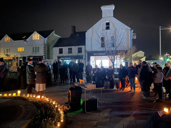 A group of people gathered at night time in Burnaby Park in Greystones standing in a circle