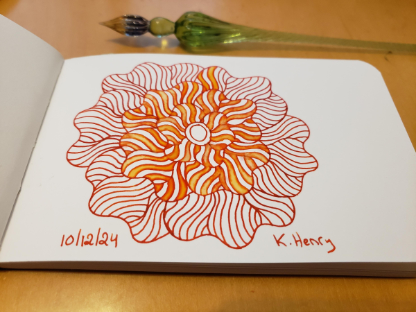 Hand drawn generative/procedural art in ink on an open page of my sketchbook. The abstract pattern is floral. My glass dipping pen is next to my sketchbook.