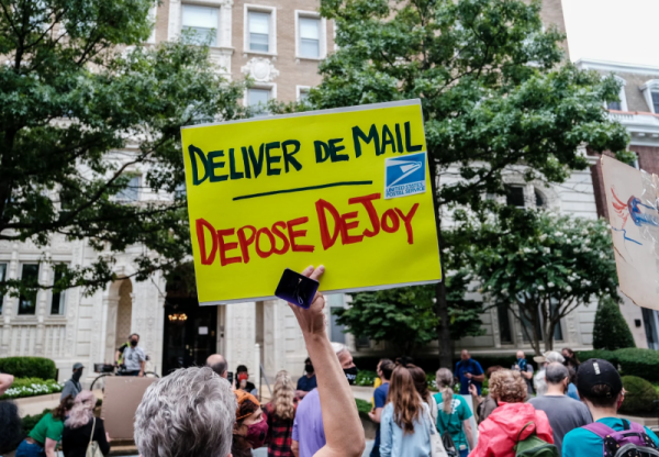 Protester holding up a sign reading, "Deliver de mail, depose DeJoy"
