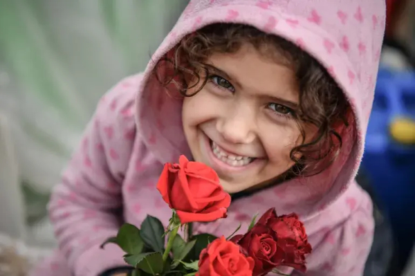 A smiling girl in pink hoodie selling red roses in Rafah, January 2024