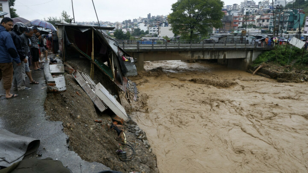 A photograph of a flooded area, with a washed out bridge. There are buildings in the background, and the water is brown.