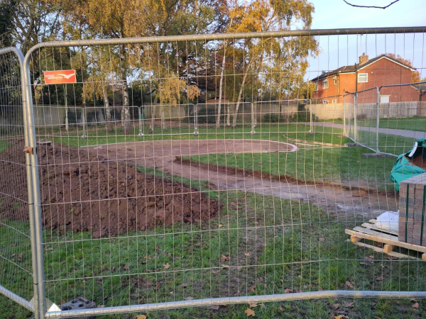 The community garden with a fence around it. There is a dirt path cutting through and a big circle in the middle.