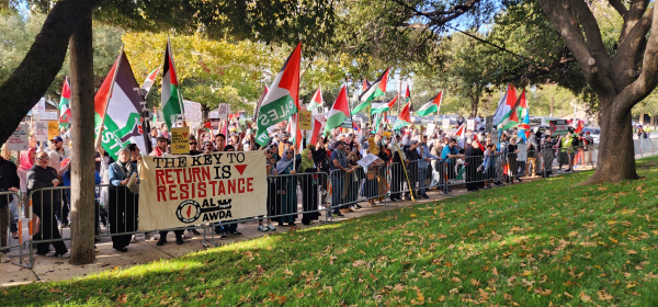 Protesters gathering at the metal barricades outside of the Hilton Anatole, with Palestinian flags and a banner that reads The Key to Return is Resistance 