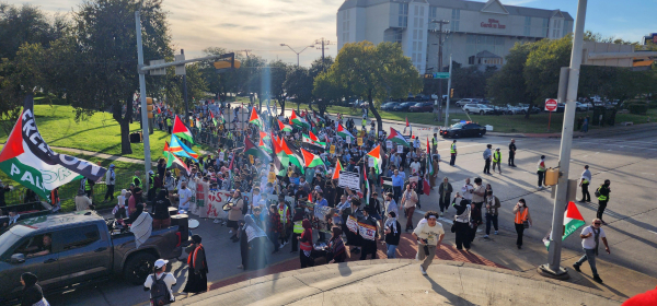 A huge crowd with banners and Palestinian flags turns onto the Frontage Road of the highway. 