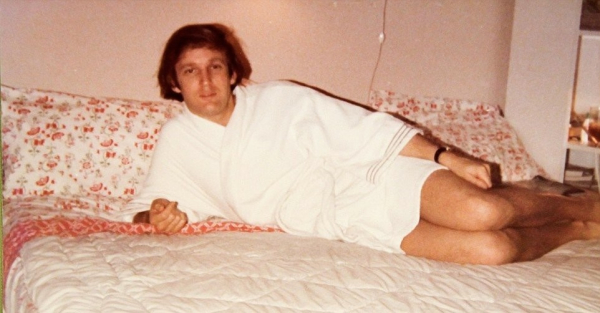 A younger Donald Trump, in his 20s, wearing a white bathrobe. He’s on a bed, and what looks like a cheaply furnished department, trying desperately to look appealing. It’s a sorry sight.