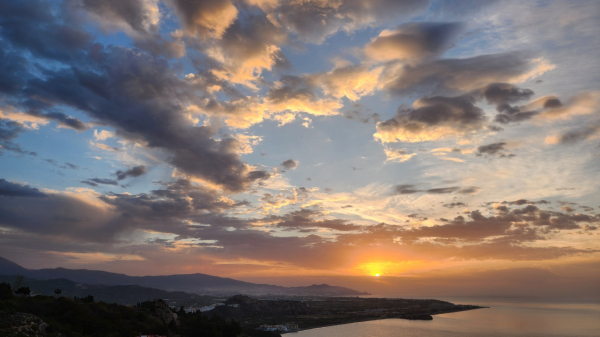 A lazy November sun, appearing in the eastern sky, peaking over the horizon of the Mediterranean Sea, firing the clouds with photonic energy. Hills rise from the south, gaining altitude towards the north. Photo taken in the west of Salobreña, Spain.