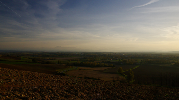 Vue sur la plaine ariégeoise au dessus de mazères en fin d'après midi. Ciel bleu brumeux avec des nuages en voilures, plaine éclairée par un soleil doré, au fond, les pyrénées et le massif du tabé ressortent de la brume