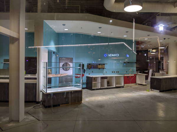 An empty storefront. The lights are still on, but there are cables hanging and empty cabinets. A lit display case holds an empty pizza box.