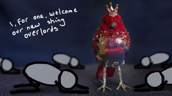 A photo of a bird ornament on a black surface, against a dark backdrop. It is facing the camera, and is made of a red velvety fabric, with a diamond encrusted gold crown and a sequined breast. It's legs are golden and glittery. It is quite something. I have added five simple drawn figures, bowed down in its glory, facing it from the left and right. In the top left is scribbled the words "I, for one, welcome our new shiny overlords".