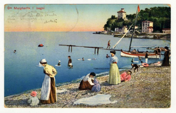 The image depicts a serene seaside scene with people engaged in various activities. In the foreground, several women and children are gathered on a rocky shoreline, dressed in vintage-style clothing that suggests an early 20th-century setting. The attire includes long skirts, dresses, aprons, and hats typical of that era.

In the middle ground, we see individuals swimming or wading in the calm waters near a pier extending into the sea. One child appears to be playing with water on the shore while another is sitting nearby. A red flag flies atop a mast connected to this wooden structure, indicating it's possibly used for anchoring boats.

The background reveals more of the picturesque seaside town with several buildings perched on cliffs overlooking the blue waters. Notable among these structures are an ornate villa or hotel and other smaller residential houses nestled amongst green foliage. The sky displays a gradient from warm yellow hues near the horizon, suggesting either sunrise or sunset, transitioning to cooler blues higher up.

A boat is moored close to one of the buildings on land, implying that boating might be another popular activity in this area. A child stands at the far right end of the pier, while other figures can be seen engaging with each other further along its length. The overall ambiance exudes leisure and relaxation typical of a day spent by the sea during an earlier era when such seaside resorts we [...]