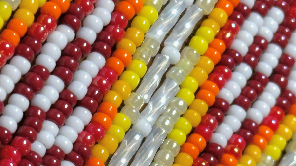 A super close-up shot of a pair of white, red, orange, and yellow beaded fringe earrings