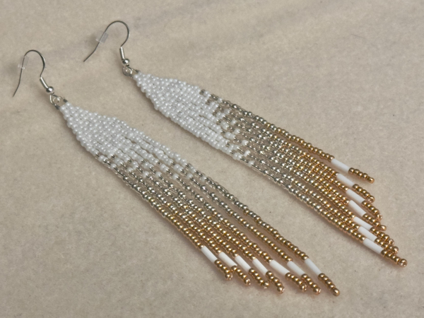 A pair of white, silver, and gold mini beaded fringe earrings on a cream colored bead mat