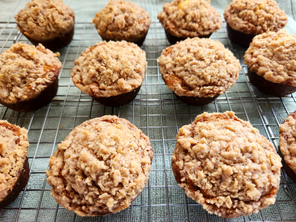 One dozen banana crumb muffins cooling on a wire rack sitting on a green kitchen towel.