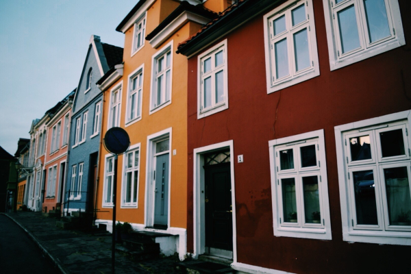 A row of colorful houses, red, blue, and yellow. A traffic sign is visible in front of the houses. 